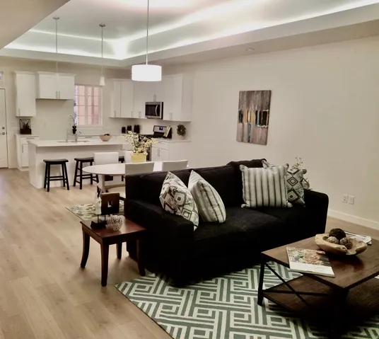 Open-concept living space featuring wood-finish flooring, recessed ceiling lighting, and a kitchen with white cabinetry, a center island with bar seating, and stainless steel appliances