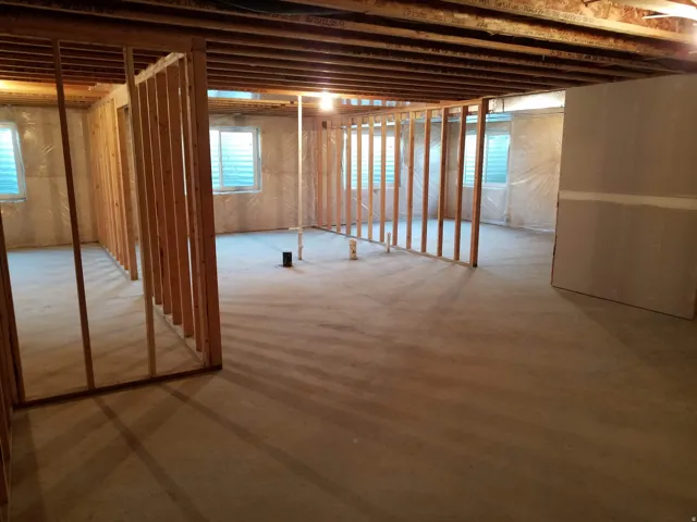 Unfinished basement featuring extensive framing, exposed ceiling joists, concrete flooring, and multiple rectangular windows