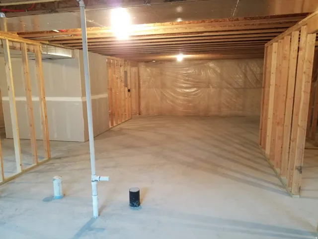 Unfinished basement with concrete flooring, exposed wood ceiling joists, and partial wood framing for future development