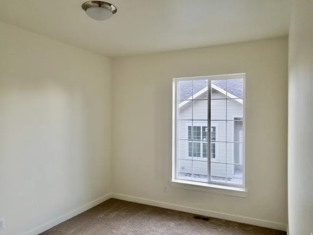Room featuring light neutral wall paint, a single window with white trim, brown carpet, and a flush-mount ceiling light fixture