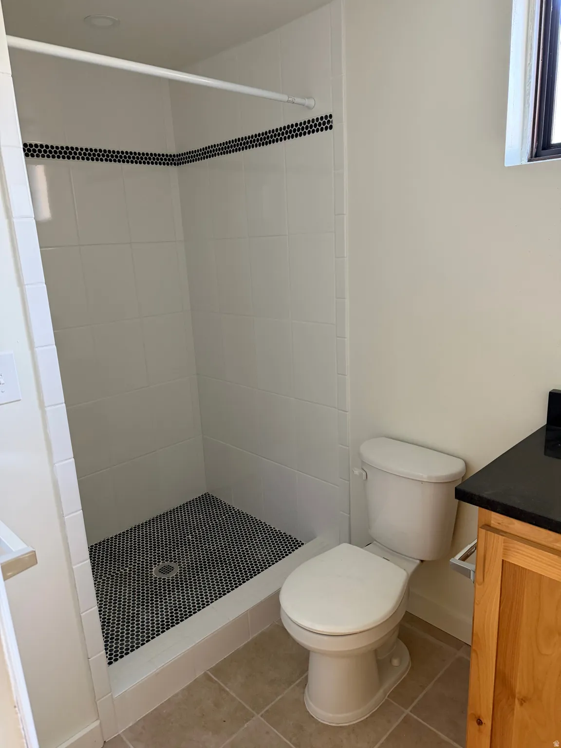 Walk-in shower with white subway tile walls, black mosaic tile floor, and a decorative black mosaic accent band