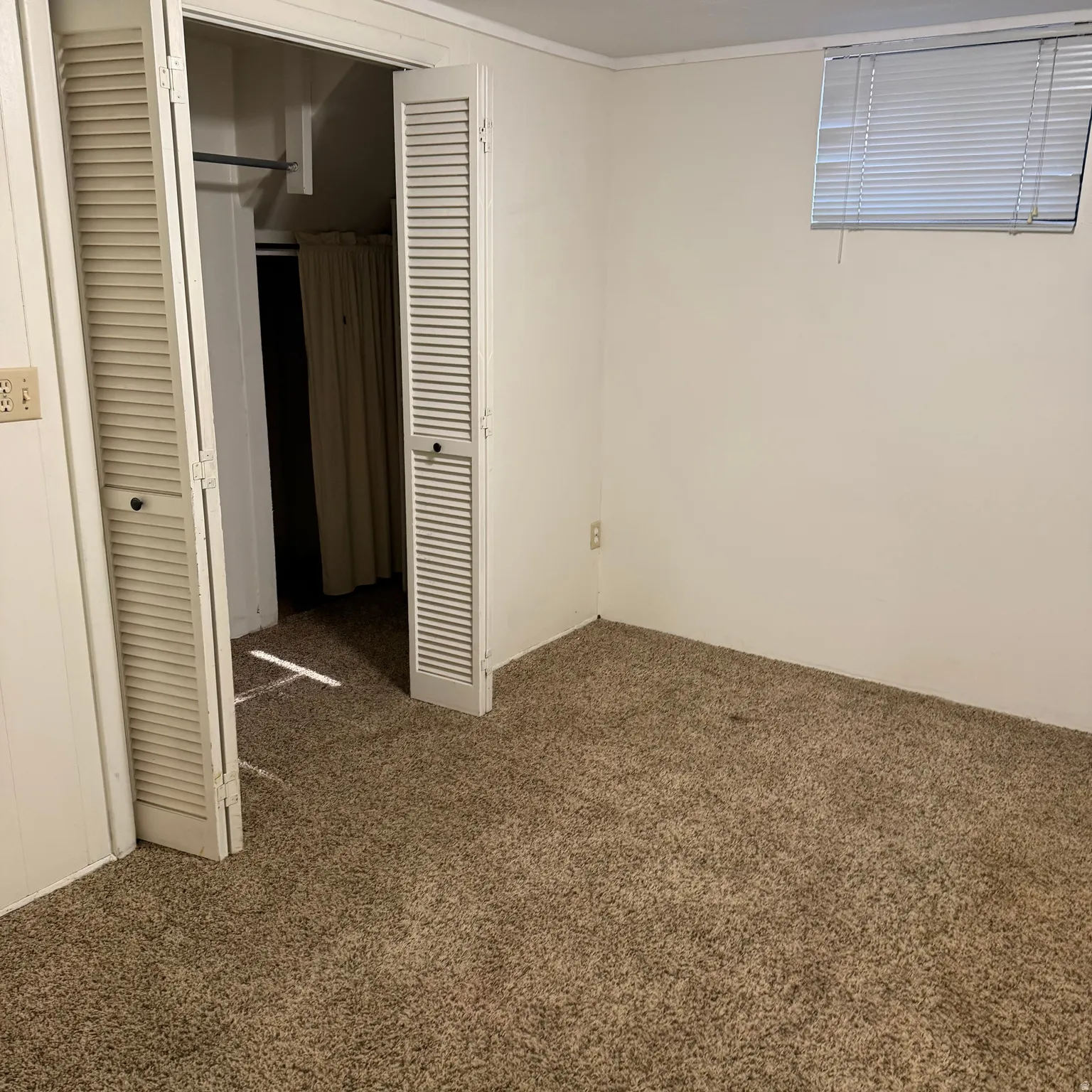 Carpeted room featuring a white painted wall finish, a window with blinds, and bi-fold louvered closet doors with a hanging rod