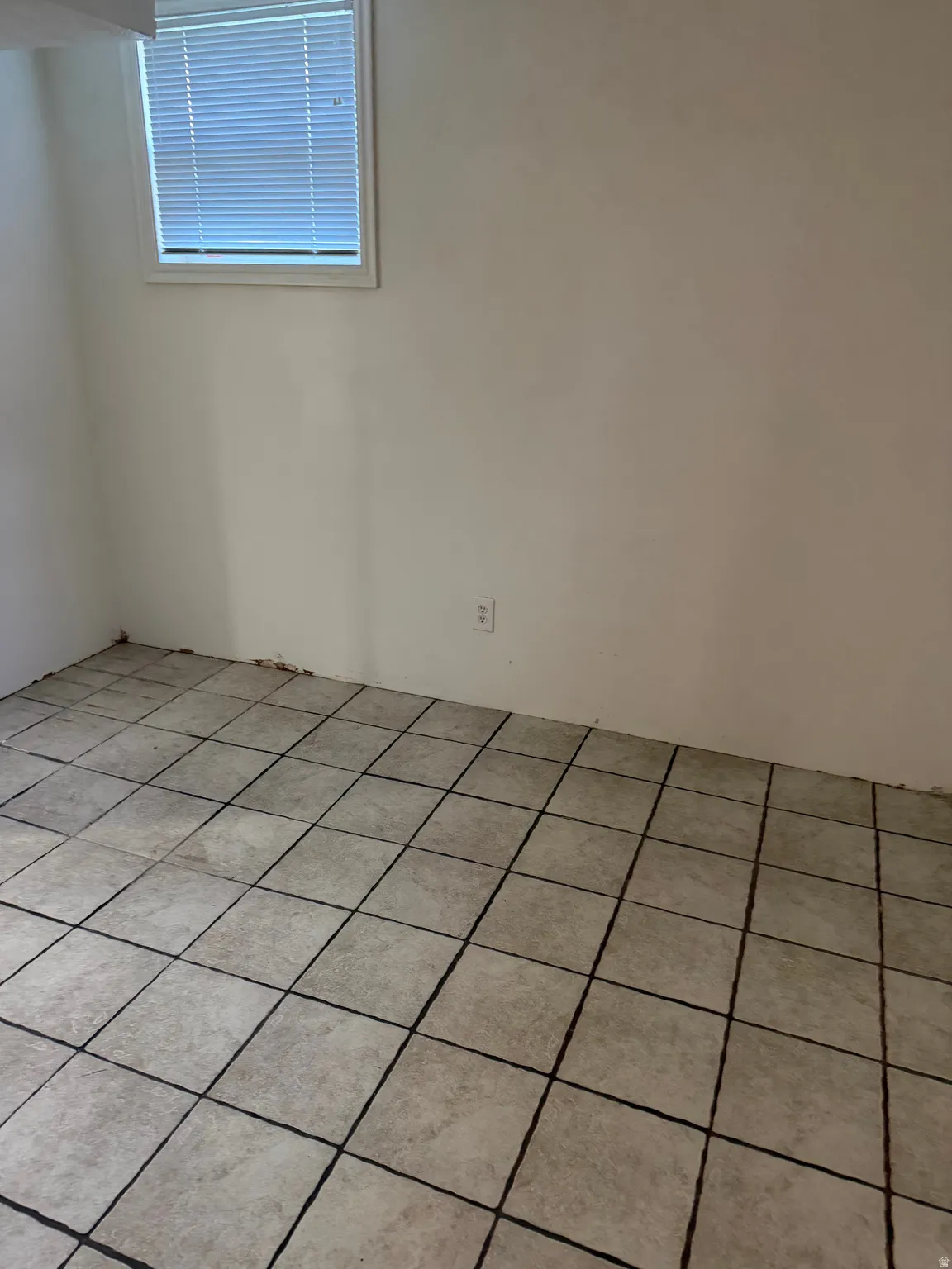 Tiled flooring featuring a grid pattern with dark grout, white walls, and a window with horizontal blinds