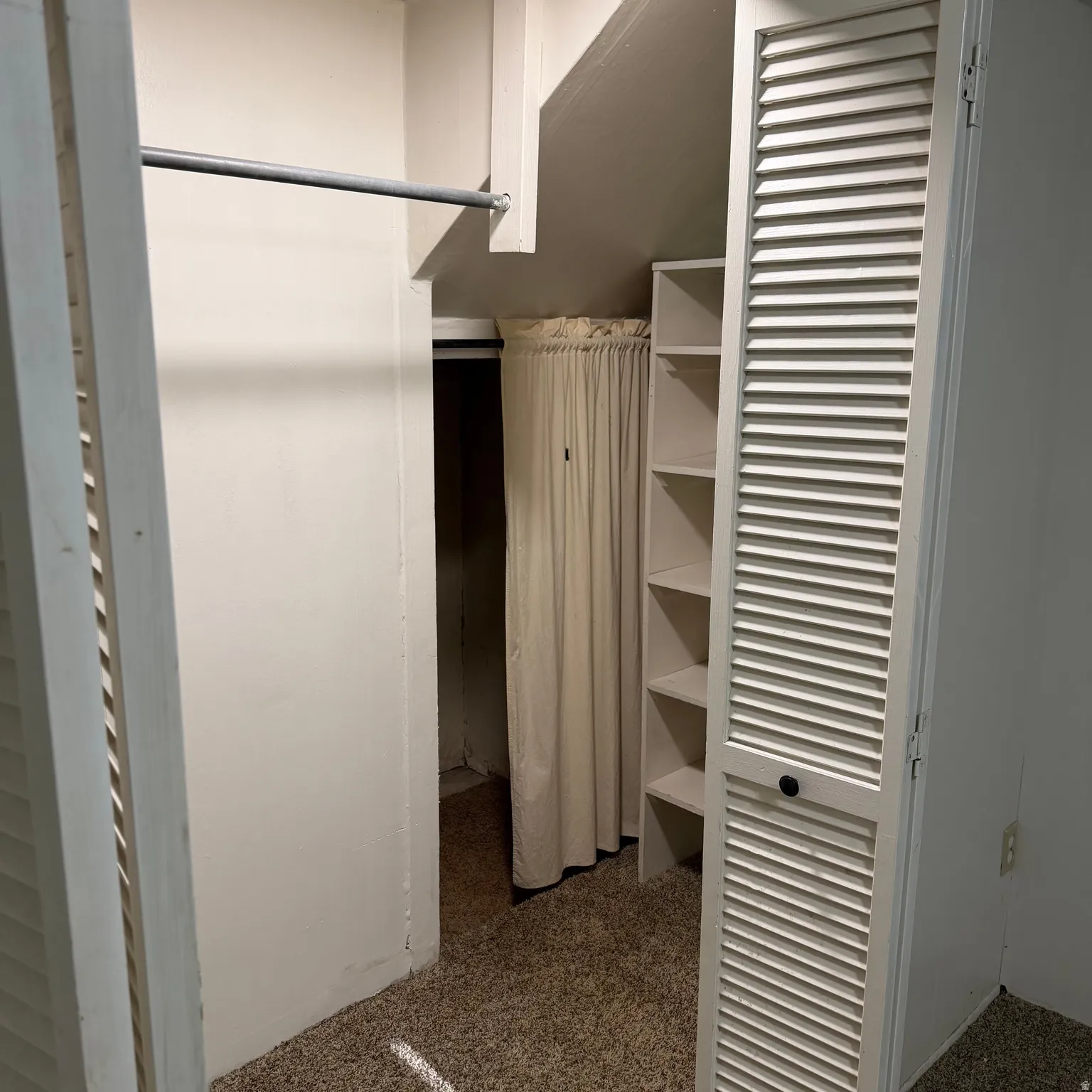 Built-in closet system featuring a hanging rod, louvered bi-fold doors, integrated shelving, and carpet flooring