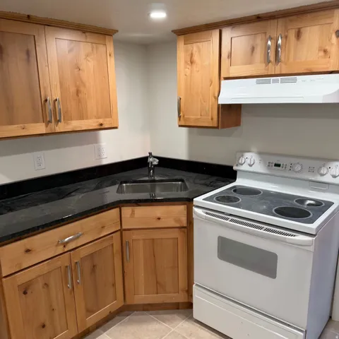Corner kitchen featuring wood cabinetry, dark countertops, and a stainless steel sink with a chrome faucet