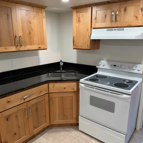 Kitchen featuring wood cabinetry, dark countertops, a stainless steel sink, a white electric range, and light-toned floor tiles