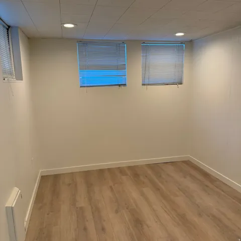 Versatile room featuring wood-finish flooring, two windows with blinds, recessed lighting, and a suspended ceiling