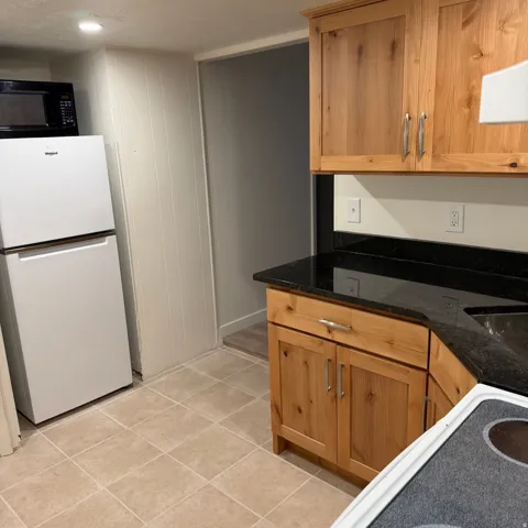 Kitchenette featuring wood-finish cabinetry, dark countertops, and tile flooring