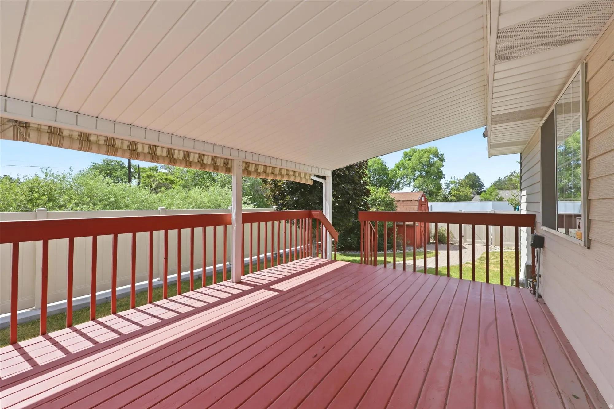 Covered outdoor deck with red-stained wood flooring and railing