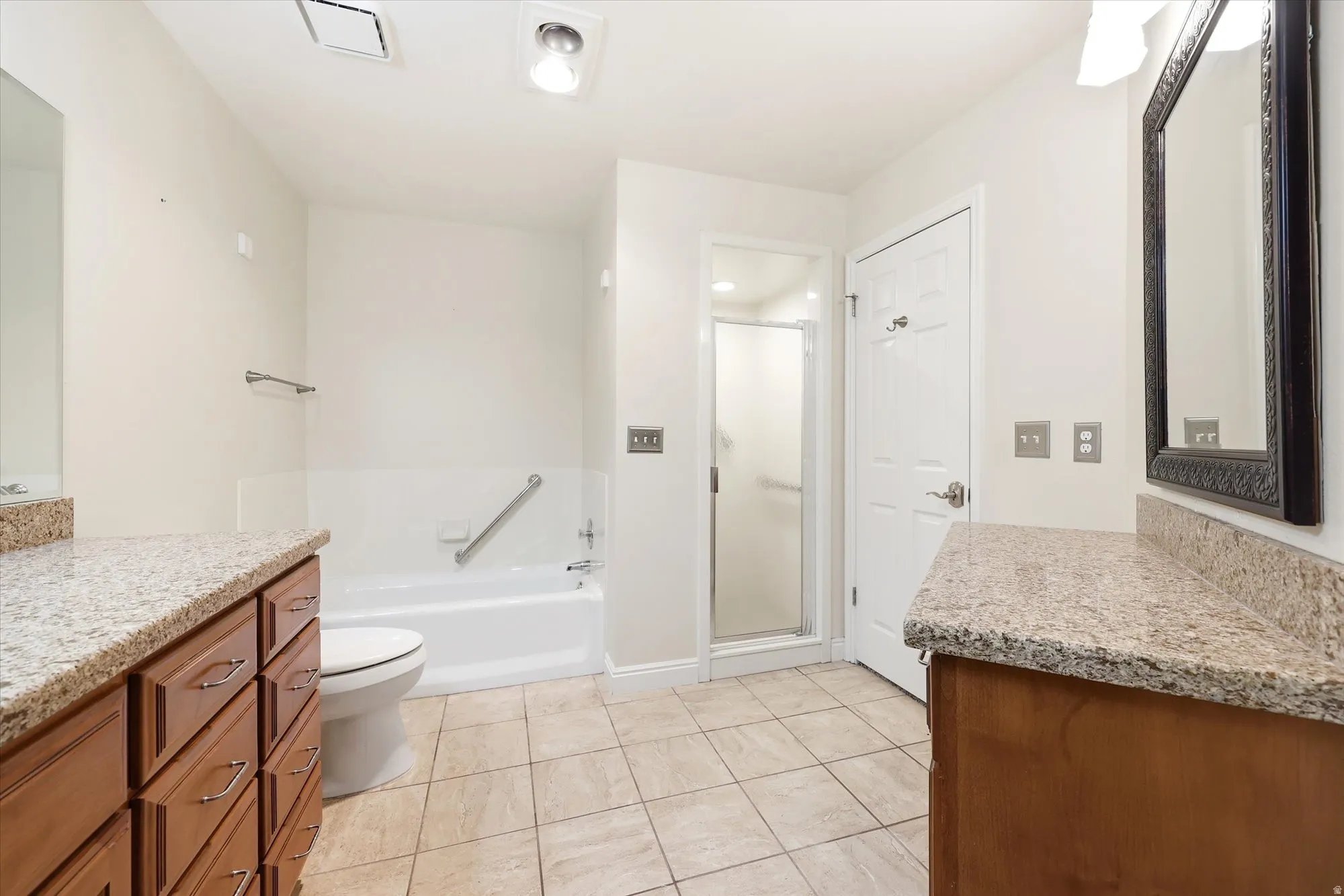 Bathroom featuring dual wood-finish vanities with stone countertops, a shower-tub combination, a separate enclosed shower, and tile flooring