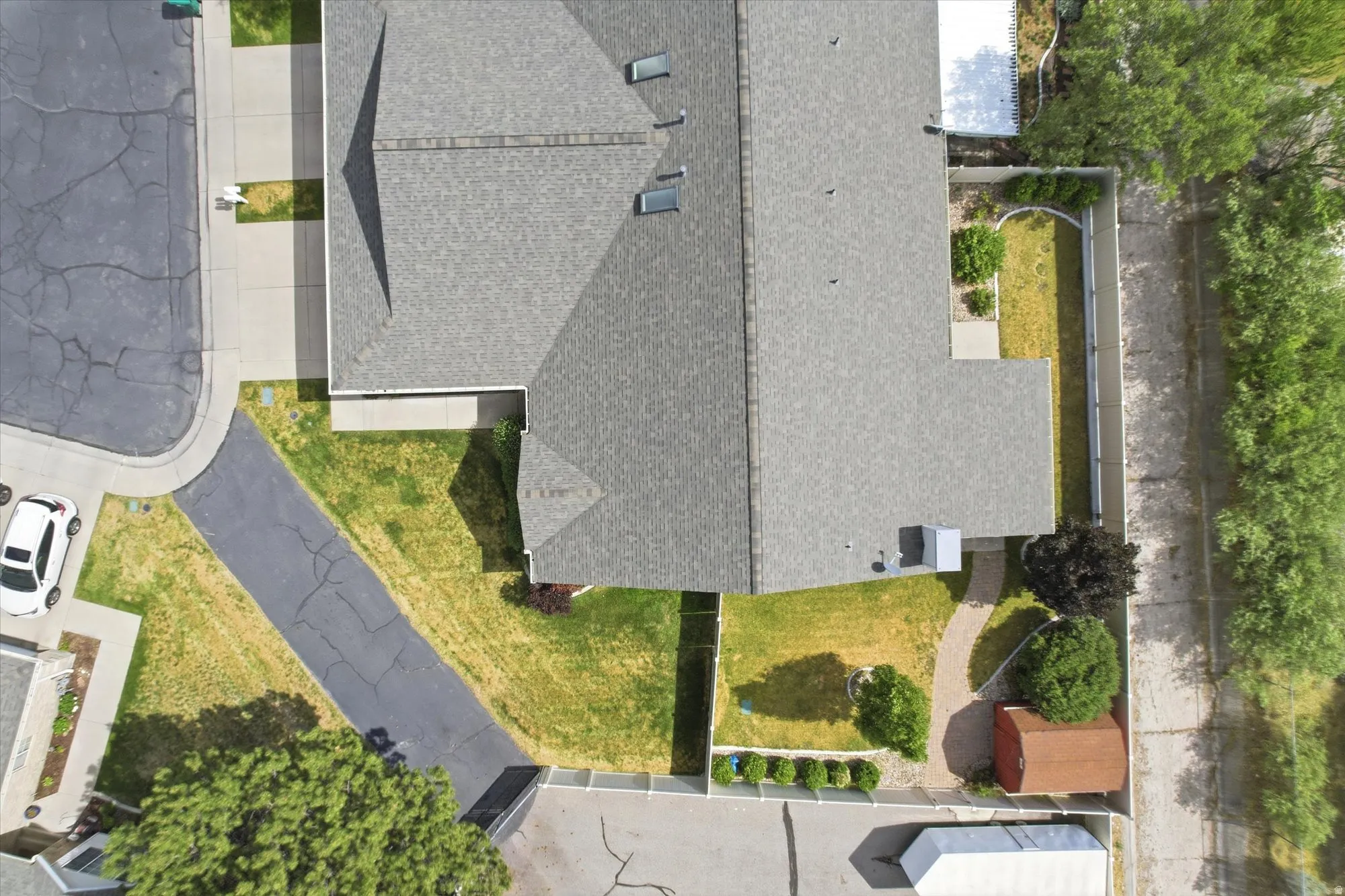 Property featuring a spacious asphalt driveway, shingled roofing, mature landscaping, and a detached storage shed