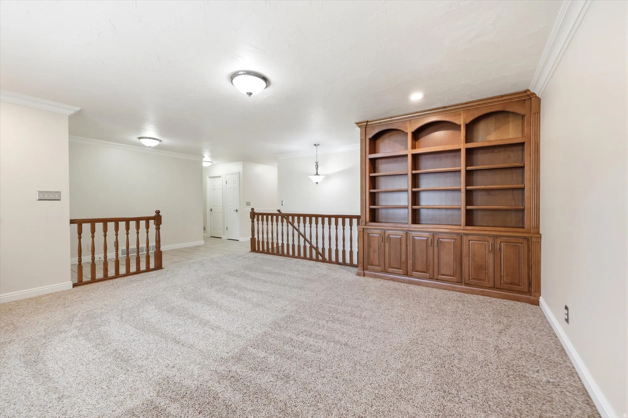 Expansive carpeted loft area featuring a large built-in wooden bookcase with arched details and lower cabinetry