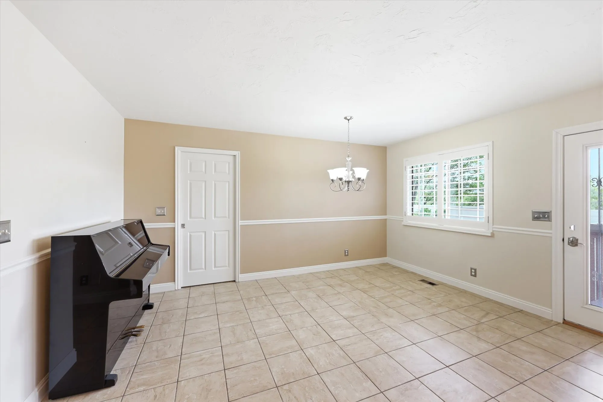 Spacious room featuring neutral tile flooring, chair rail molding, and a chandelier light fixture