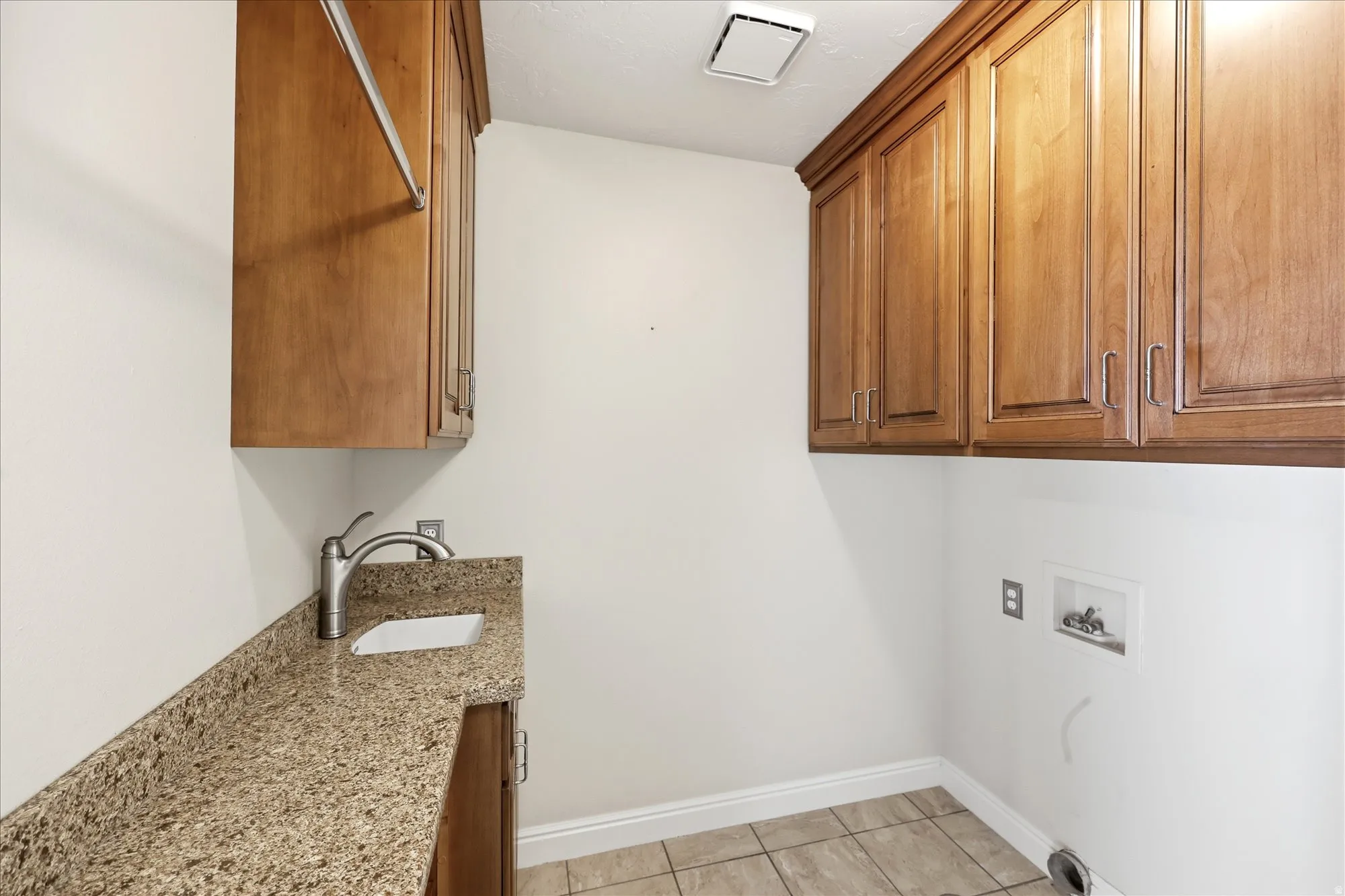 Laundry room featuring extensive wood cabinetry, a utility sink with a stone countertop, a built-in hanging rod, and tile flooring