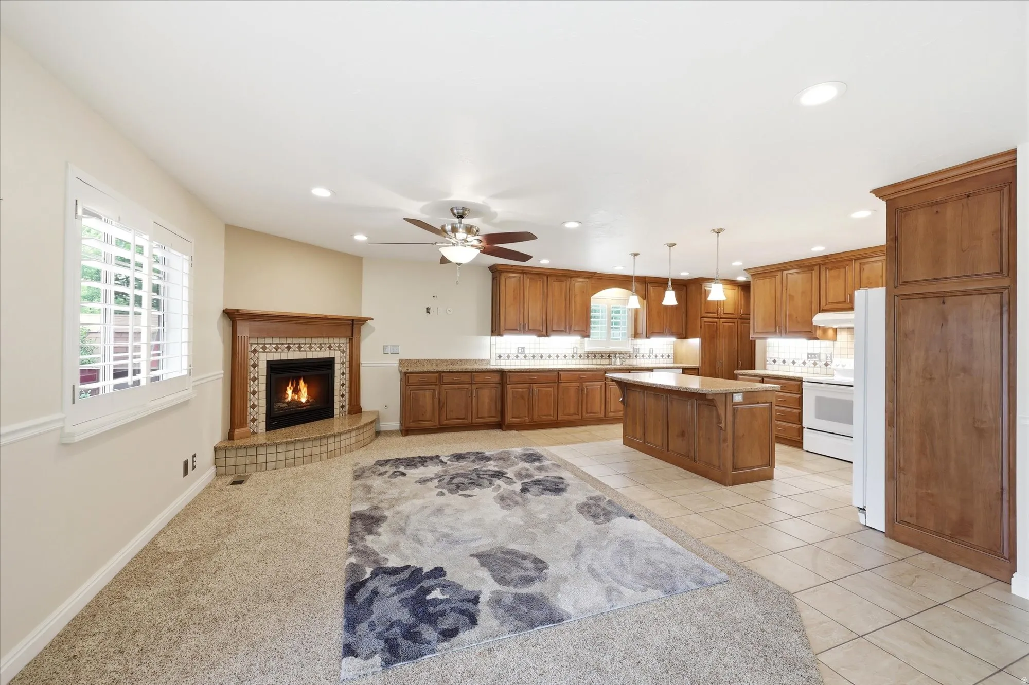 Open-concept living area featuring a corner fireplace with tile surround, wood mantel, and hearth
