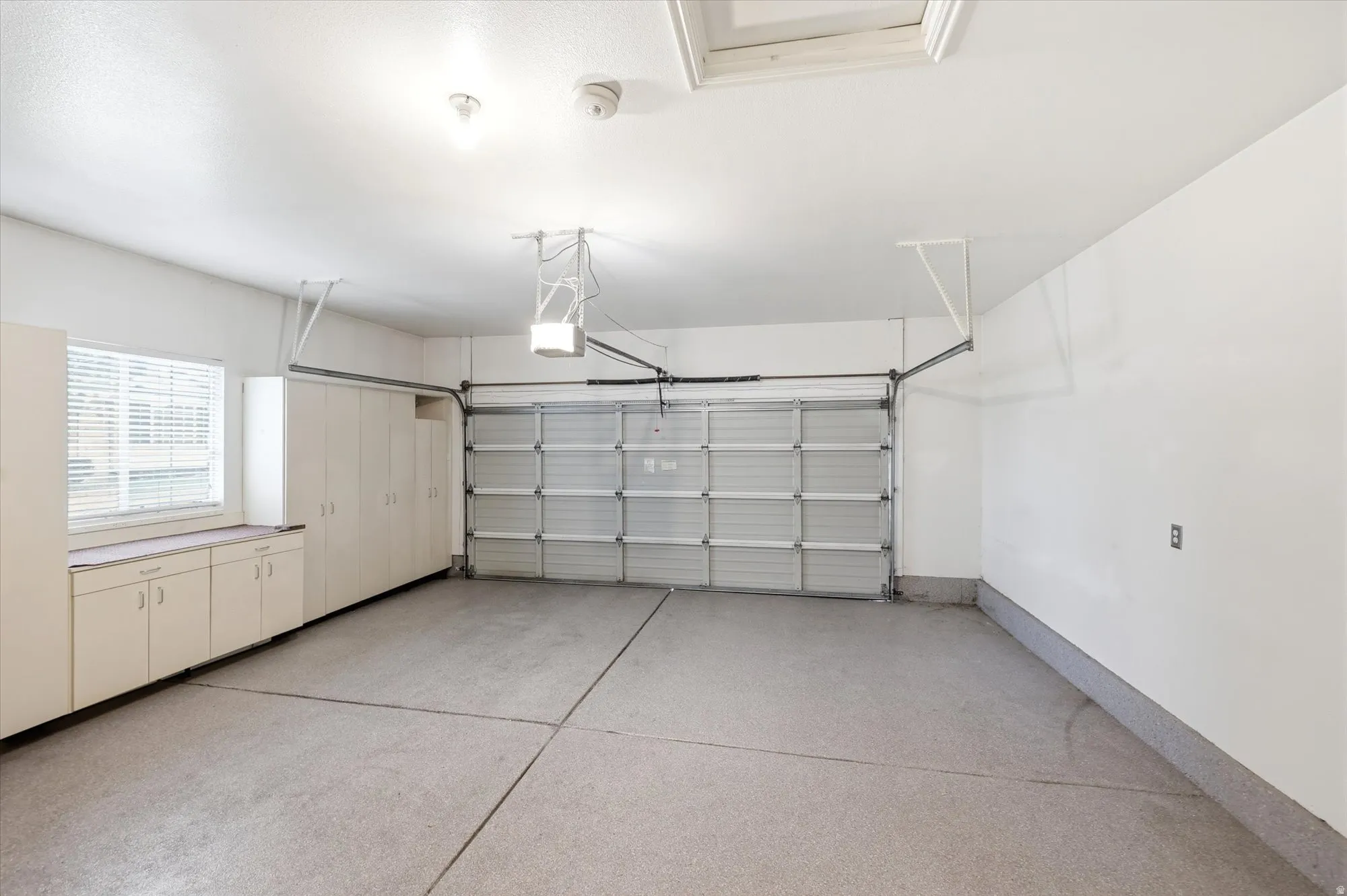 Spacious garage with an epoxy-coated floor, integrated storage cabinetry, built-in workbench with surface, a window with blinds, and an overhead garage door opener