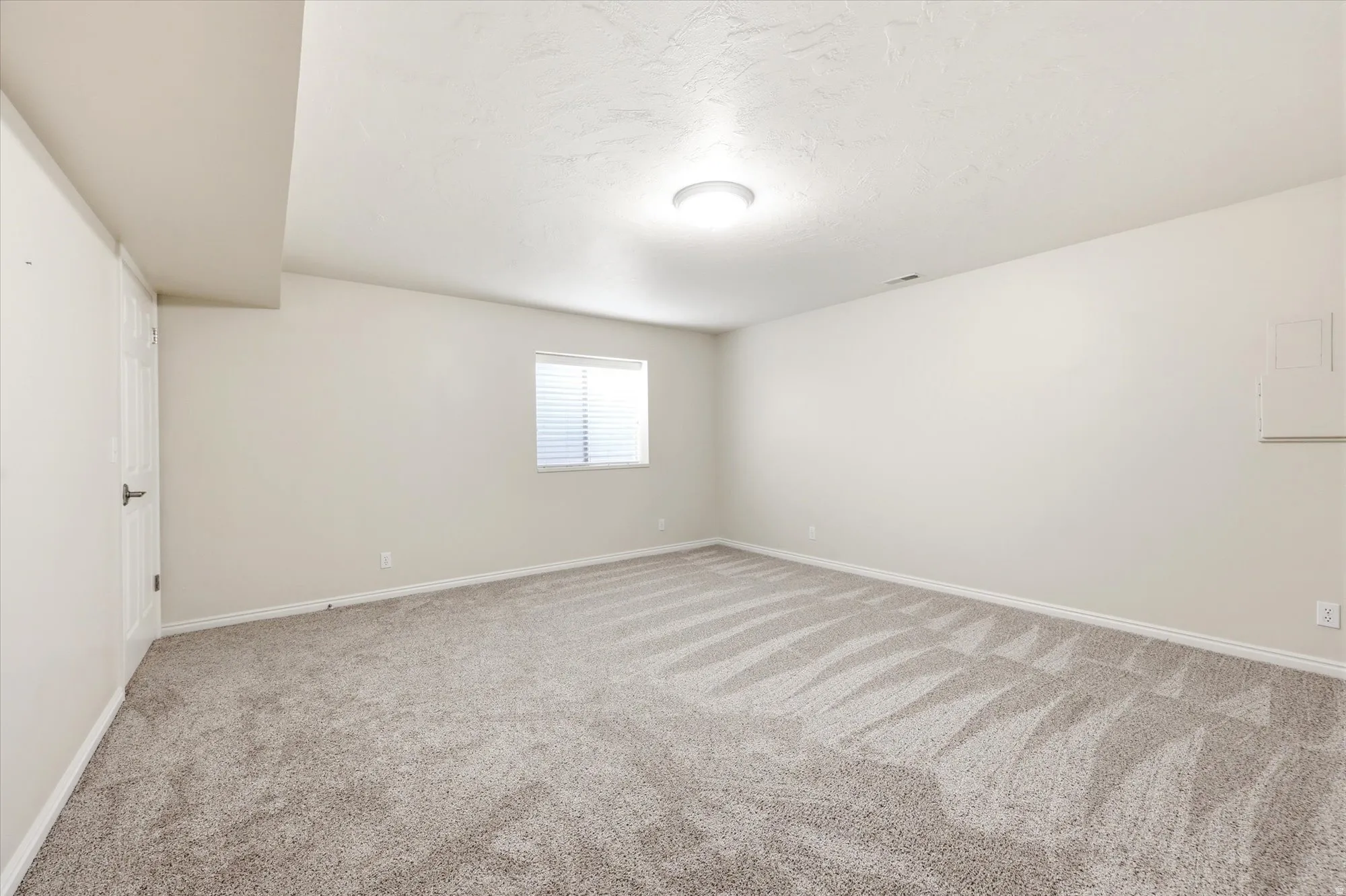 Spacious room featuring neutral carpeting, light-toned walls, and a window with horizontal blinds