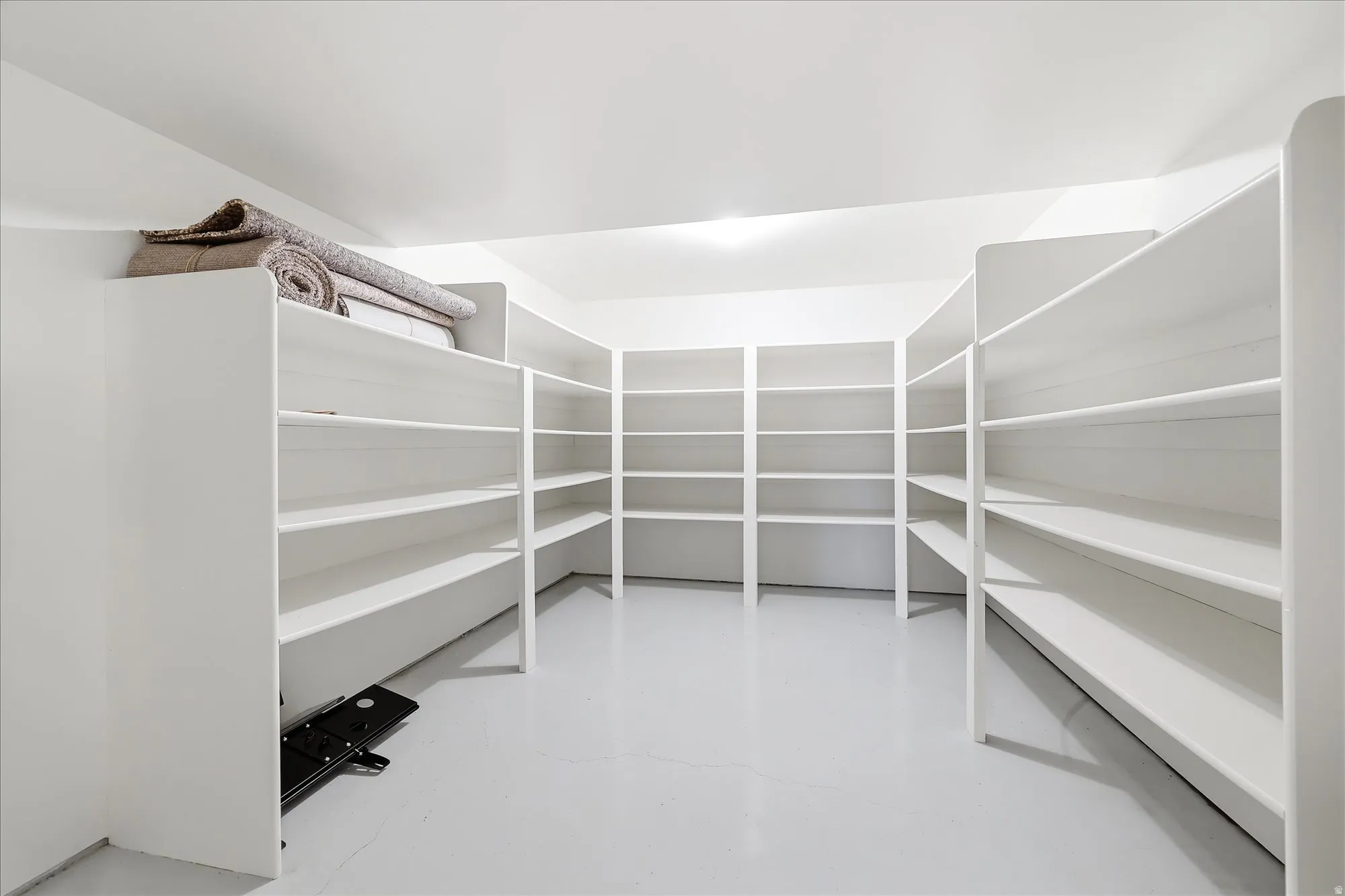 Dedicated storage room featuring extensive built-in shelving, white painted walls, and light-toned flooring