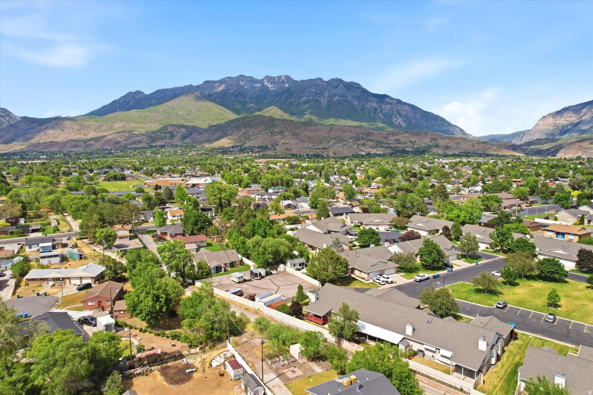 Mountain backdrop with a residential area featuring numerous mature trees and a clear sky