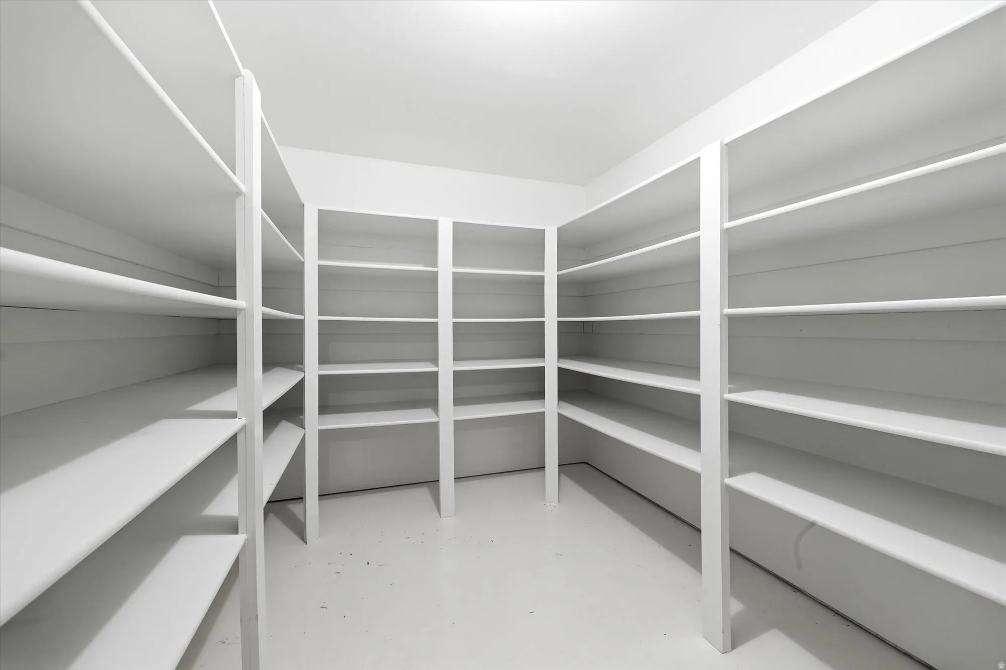 Spacious walk-in pantry featuring white shelving units on multiple walls, providing extensive storage capacity