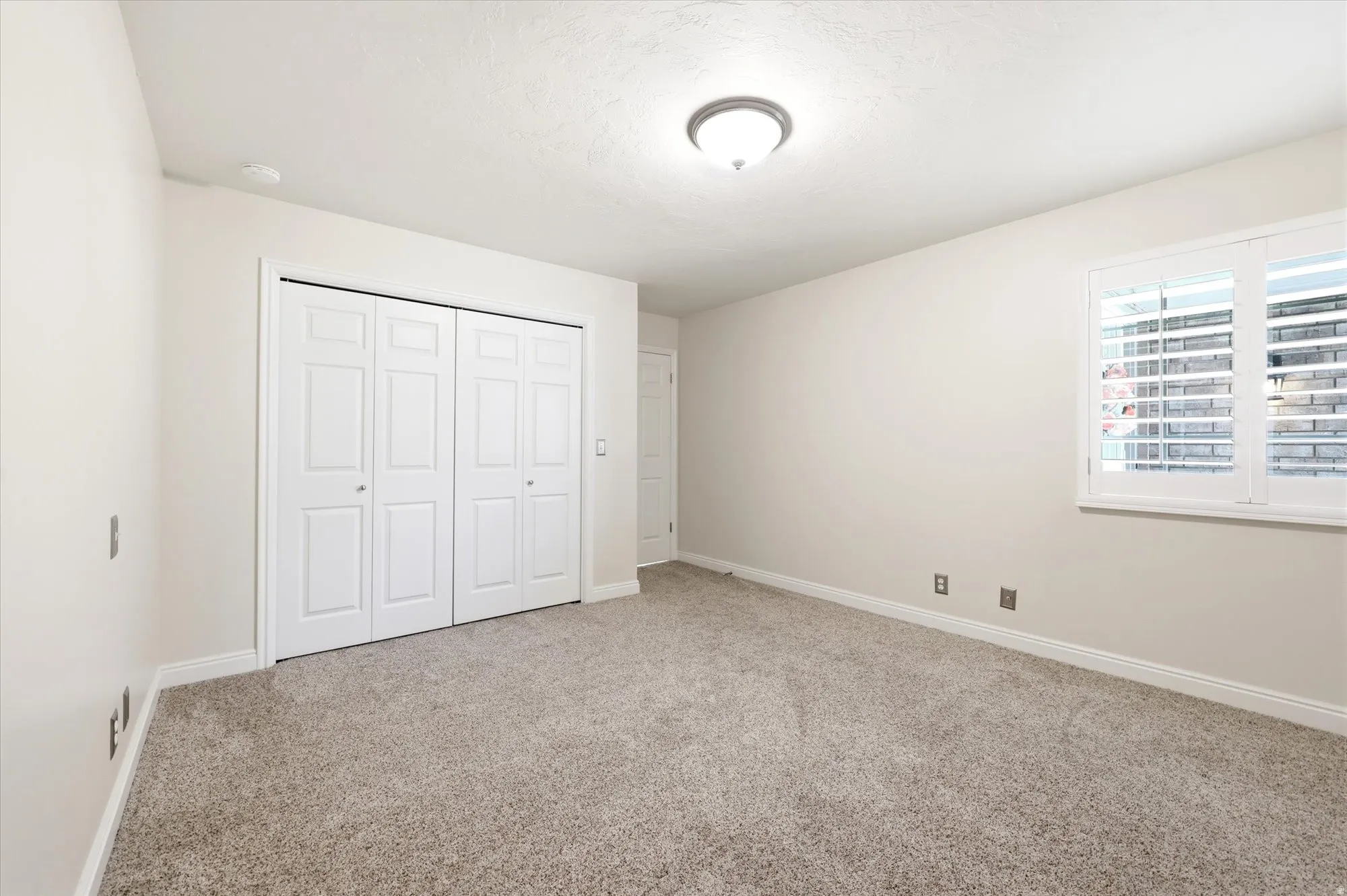 Carpeted room with a double bi-fold closet, white trim, and a window featuring white plantation shutters