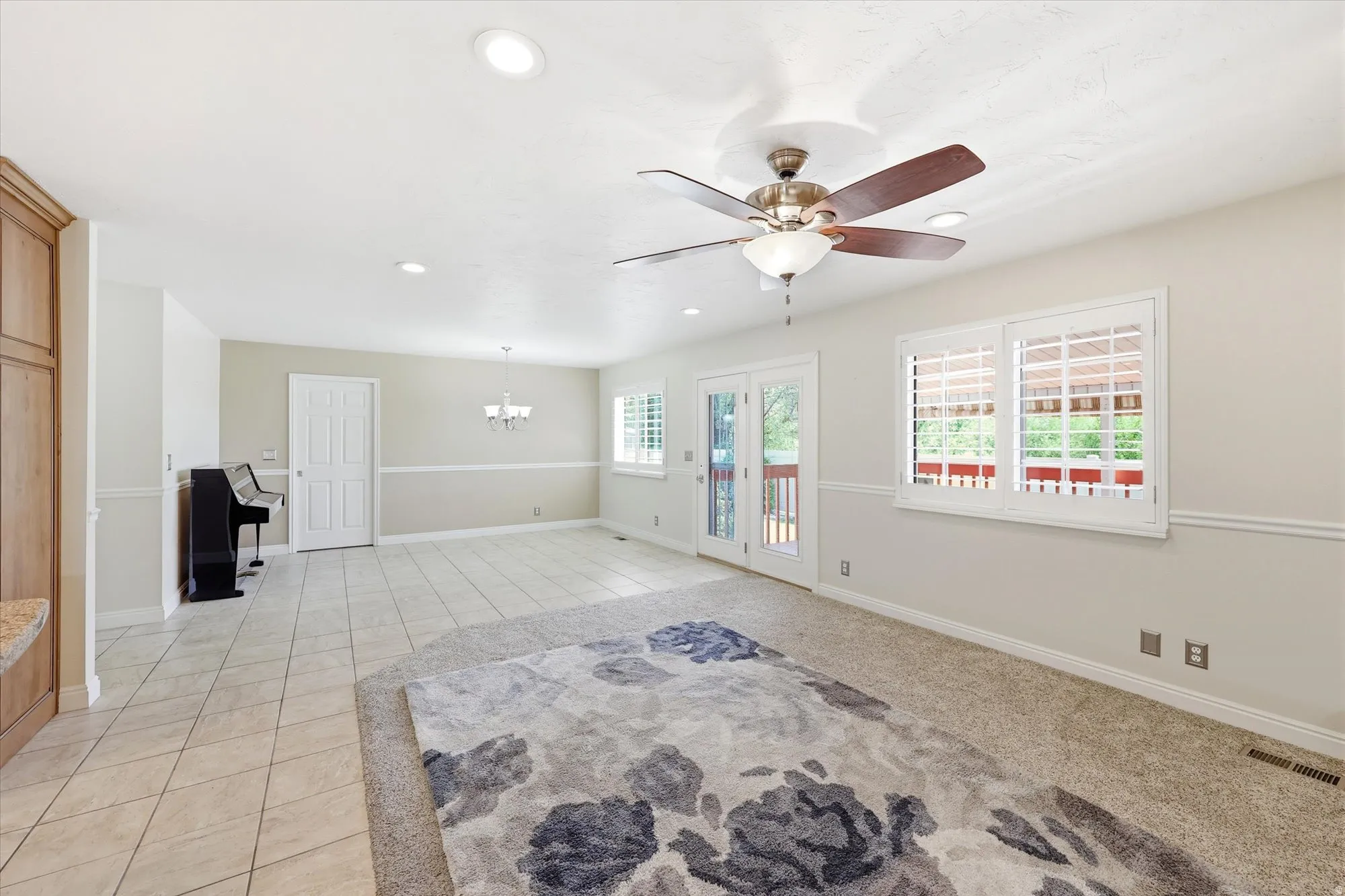 Spacious room featuring a mix of tile flooring and carpeting, double French doors, large windows with plantation shutters, a ceiling fan with integrated lighting, and recessed ceiling lights