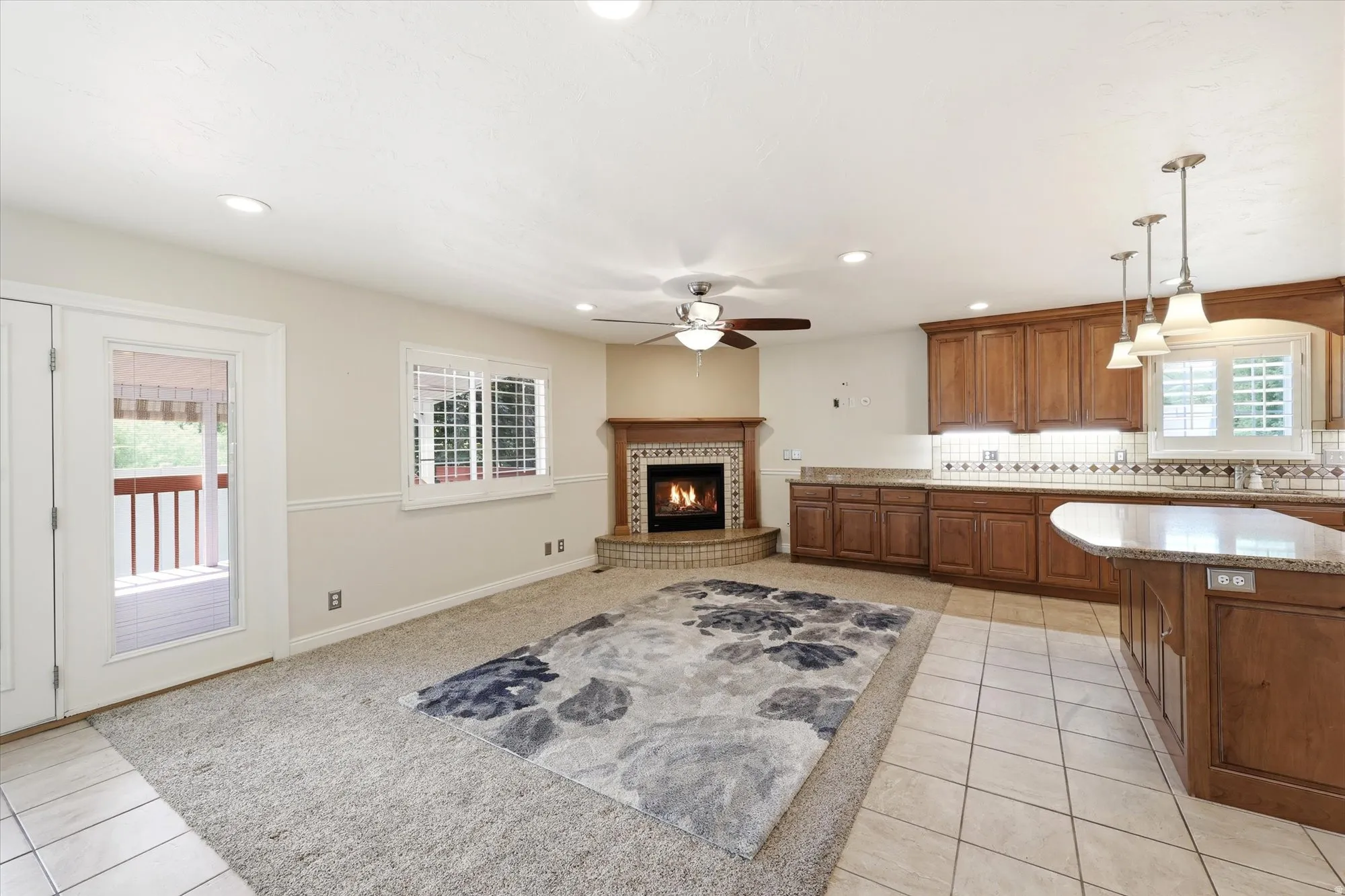 Open-concept living space featuring a corner fireplace with a decorative tile surround and wood mantle, wood cabinetry, granite countertops, and tile flooring