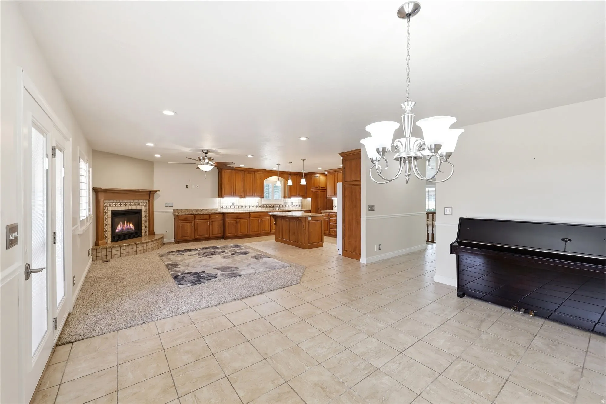 Open-concept space featuring ceramic tile flooring, a fireplace with a decorative mantel and hearth, warm-toned wood cabinetry, and a ceiling fan