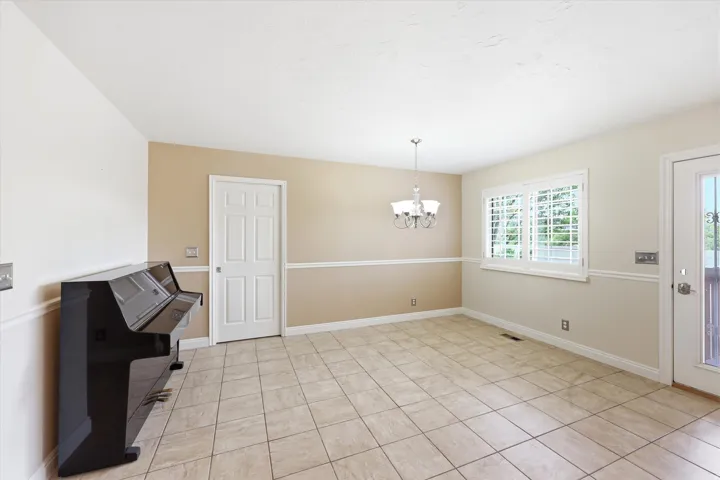 Spacious room featuring neutral tile flooring, chair rail molding, and a chandelier light fixture
