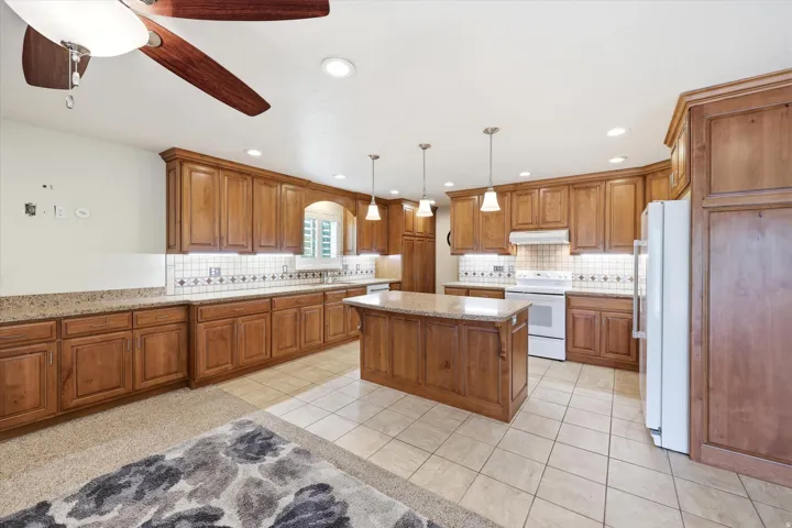 Spacious kitchen featuring extensive wood cabinetry, a central island with a granite-style countertop, recessed lighting, tile flooring, and a decorative tile backsplash