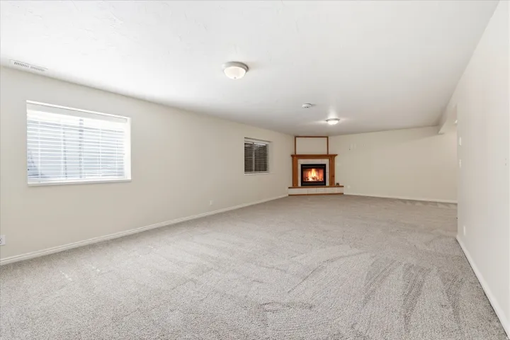 Spacious room featuring light-toned carpet flooring, neutral painted walls, and a corner fireplace with a wood mantle