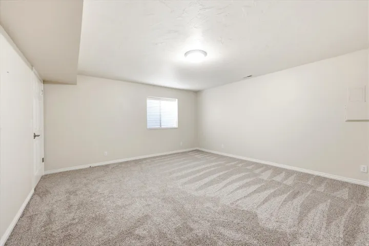 Spacious room featuring neutral carpeting, light-toned walls, and a window with horizontal blinds