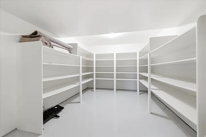 Dedicated storage room featuring extensive built-in shelving, white painted walls, and light-toned flooring