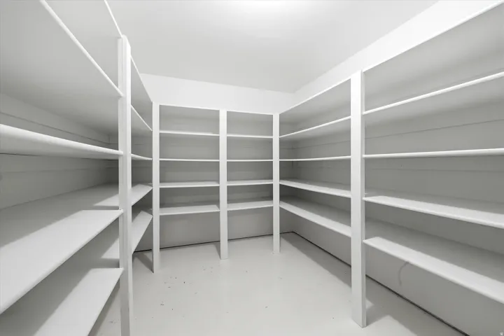 Spacious walk-in pantry featuring white shelving units on multiple walls, providing extensive storage capacity