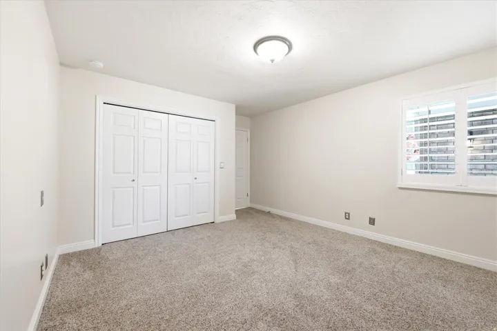 Carpeted room with a double bi-fold closet, white trim, and a window featuring white plantation shutters