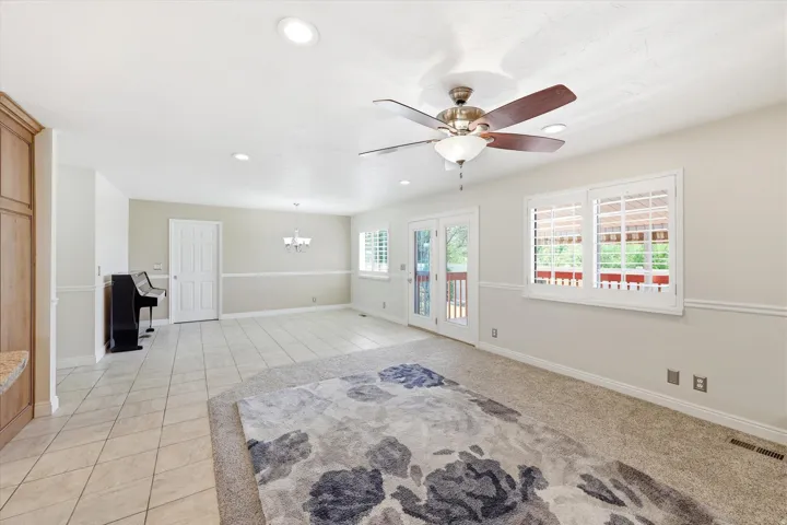 Spacious room featuring a mix of tile flooring and carpeting, double French doors, large windows with plantation shutters, a ceiling fan with integrated lighting, and recessed ceiling lights