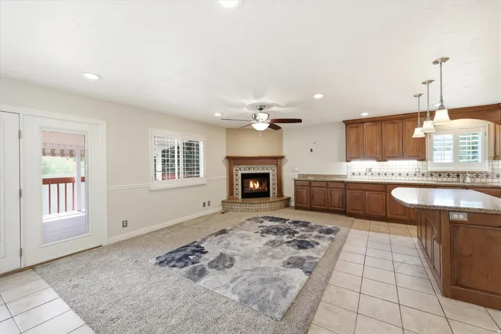 Open-concept living space featuring a corner fireplace with a decorative tile surround and wood mantle, wood cabinetry, granite countertops, and tile flooring