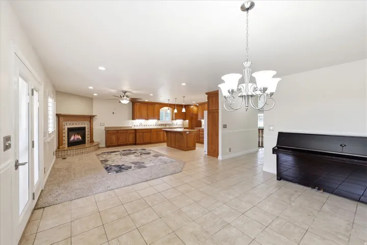 Open-concept space featuring ceramic tile flooring, a fireplace with a decorative mantel and hearth, warm-toned wood cabinetry, and a ceiling fan