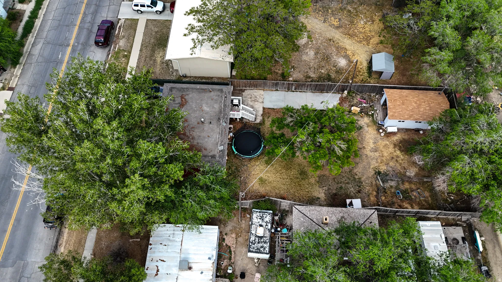 Spacious property featuring a main structure with a flat roof, a secondary structure with a shingled roof, a paved driveway, and mature trees