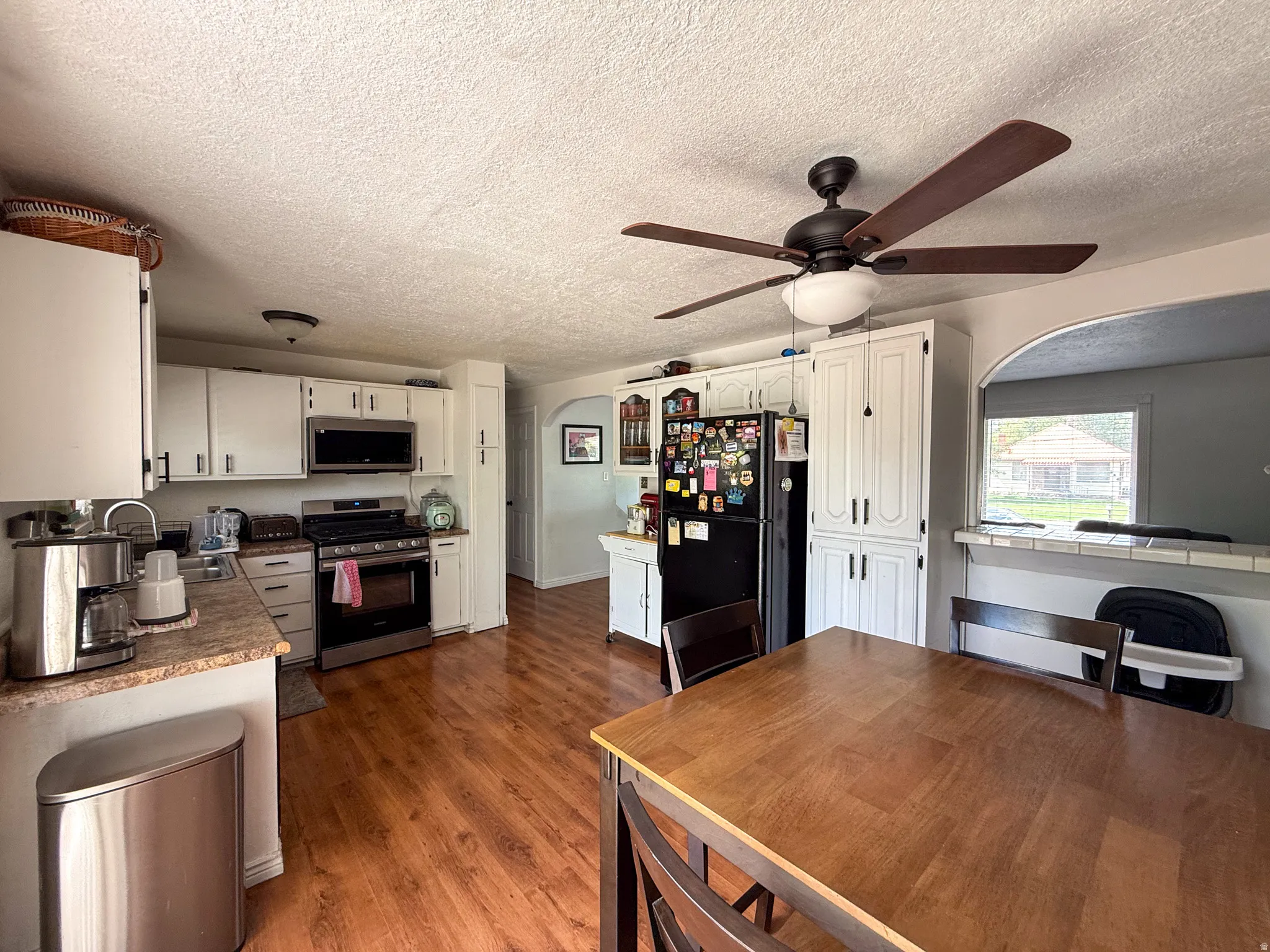 Kitchen with wood-finish flooring, white cabinetry, stainless steel appliances, and a ceiling fan