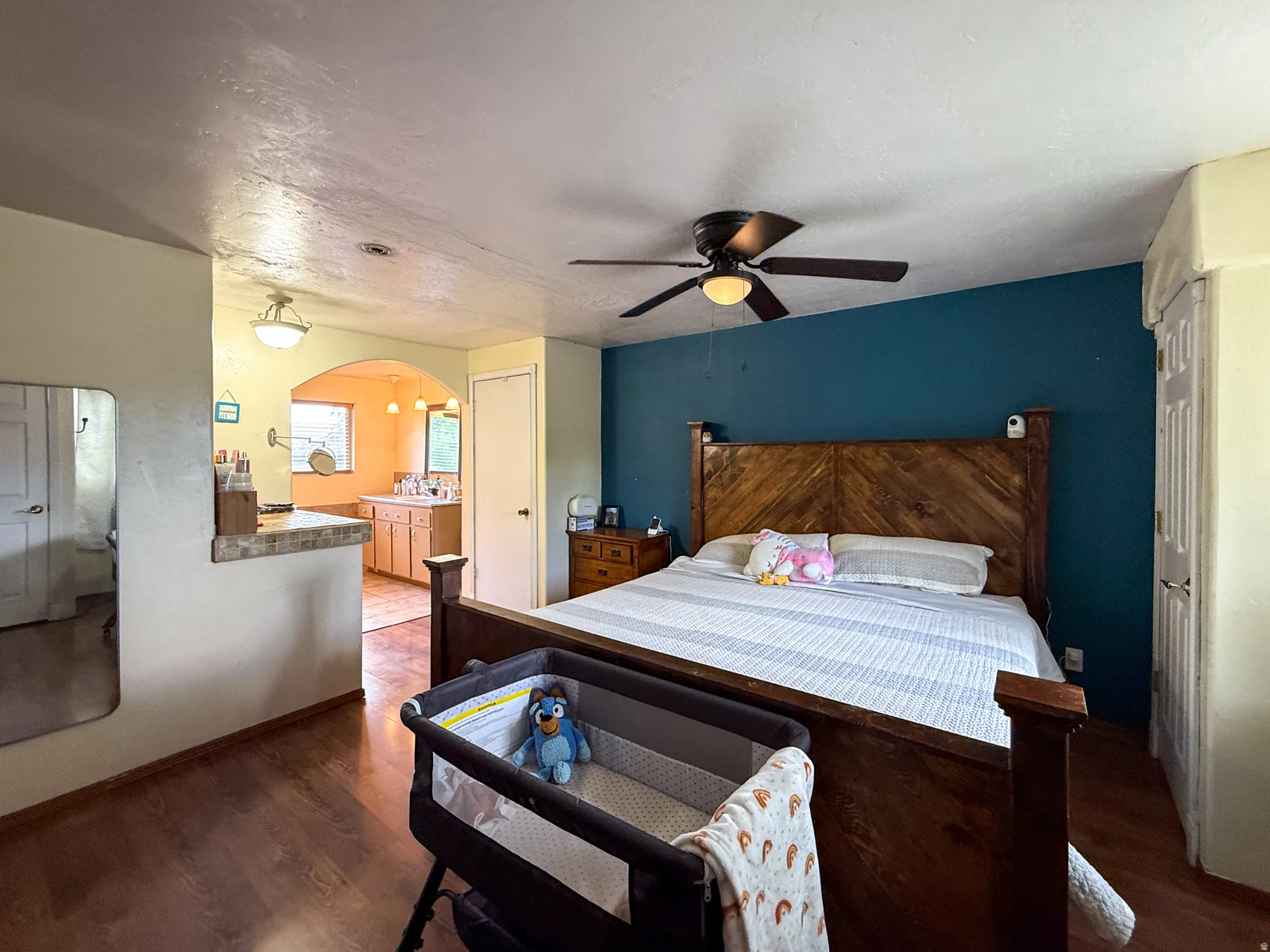 Spacious room featuring wood-finish flooring, a ceiling fan with integrated lighting, and an arched doorway leading to a bathroom