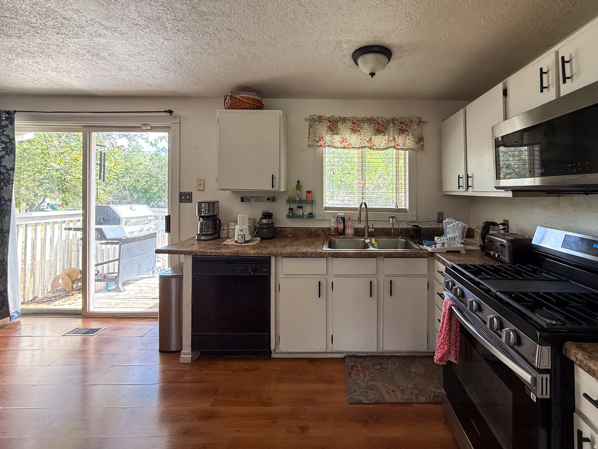 Kitchen featuring white cabinetry, wood-finish flooring, a stainless steel gas range, and a dual basin sink