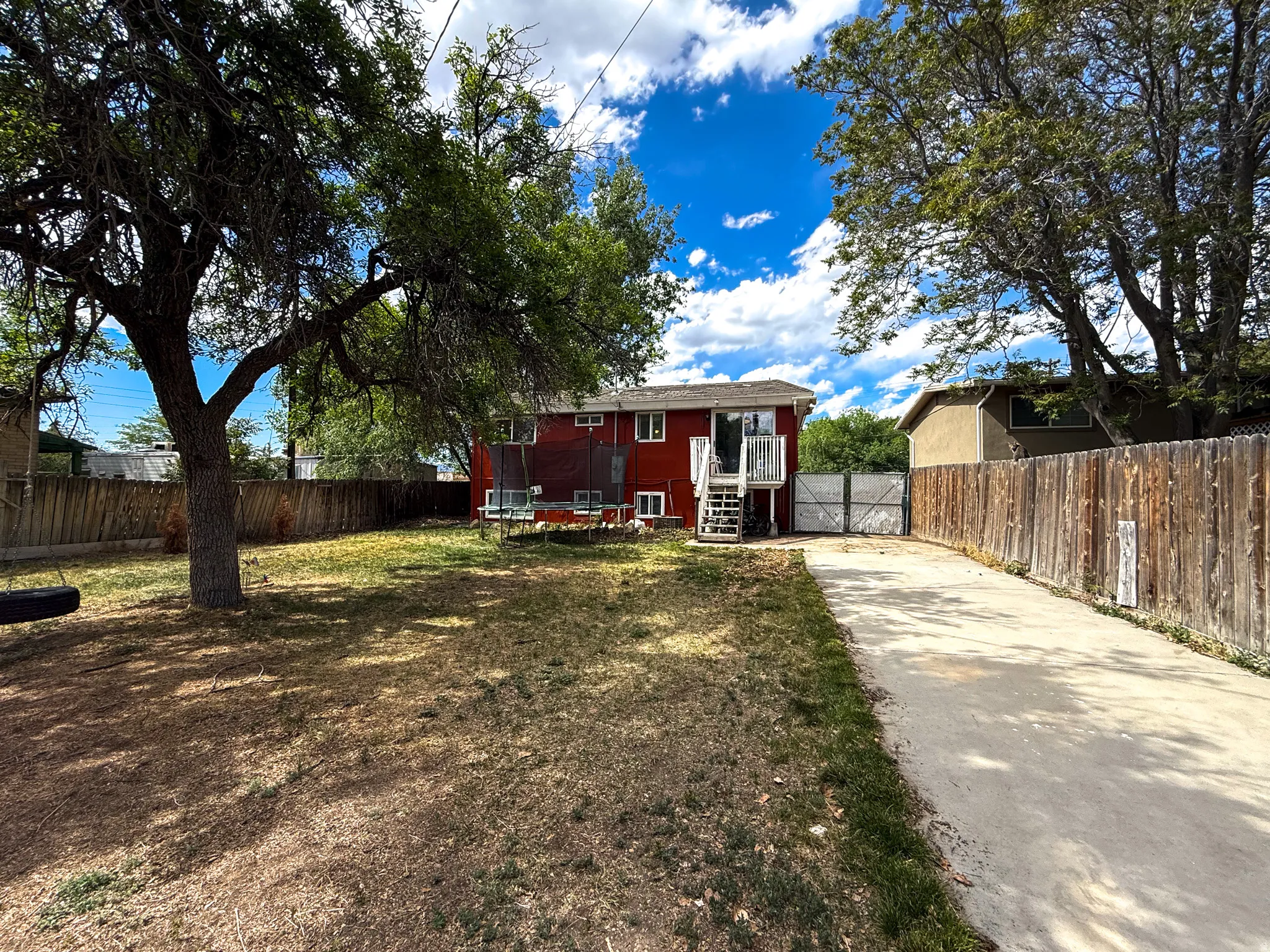 Expansive backyard featuring mature trees, a concrete driveway, and a wood privacy fence