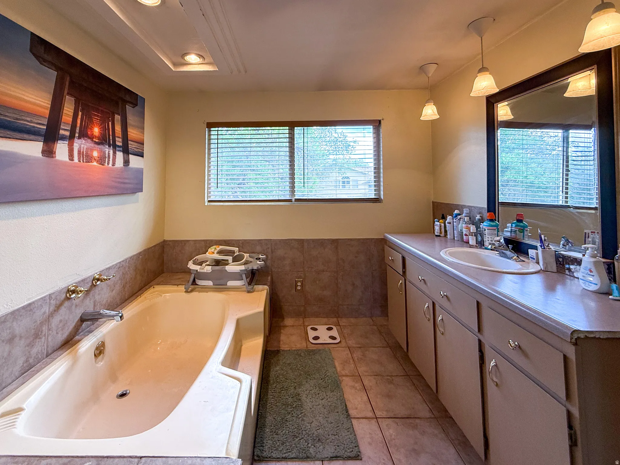 Soaking tub with brass fixtures, tile surround, and an overhead recessed light