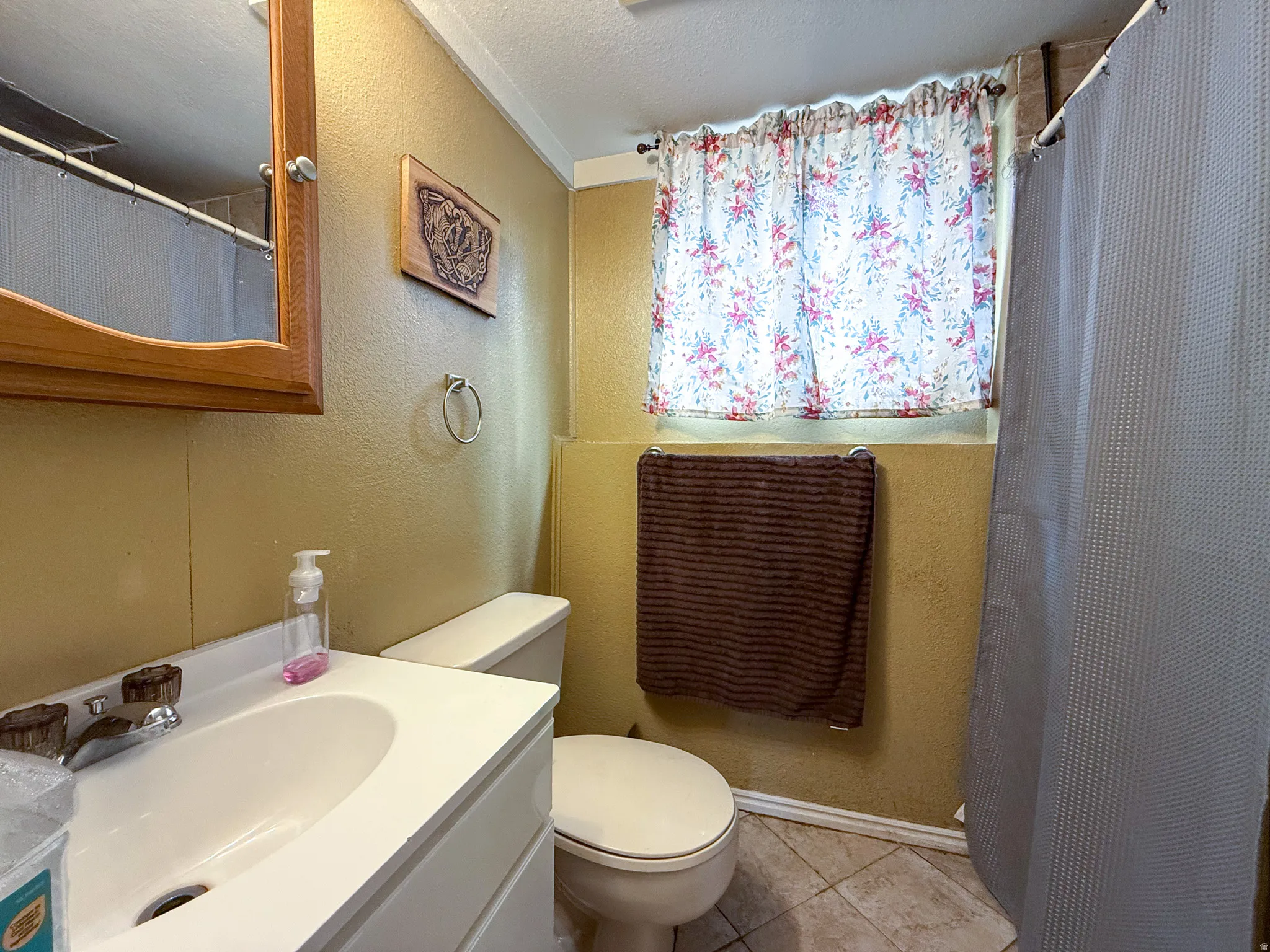 Bathroom featuring a white vanity with integrated sink, a toilet, and a tiled floor