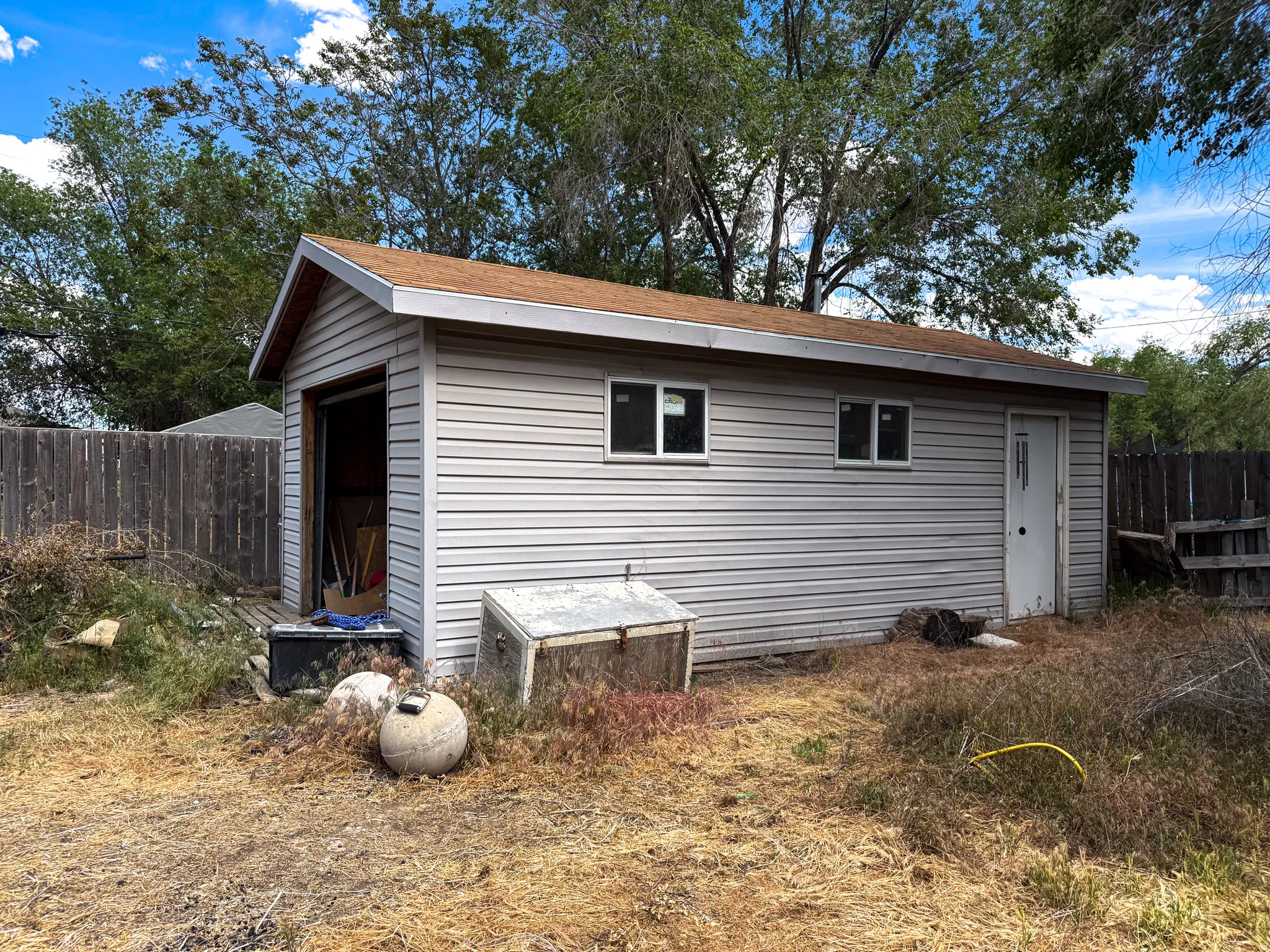 Detached shed featuring horizontal siding, a shingle roof, dual windows, and an overhead door