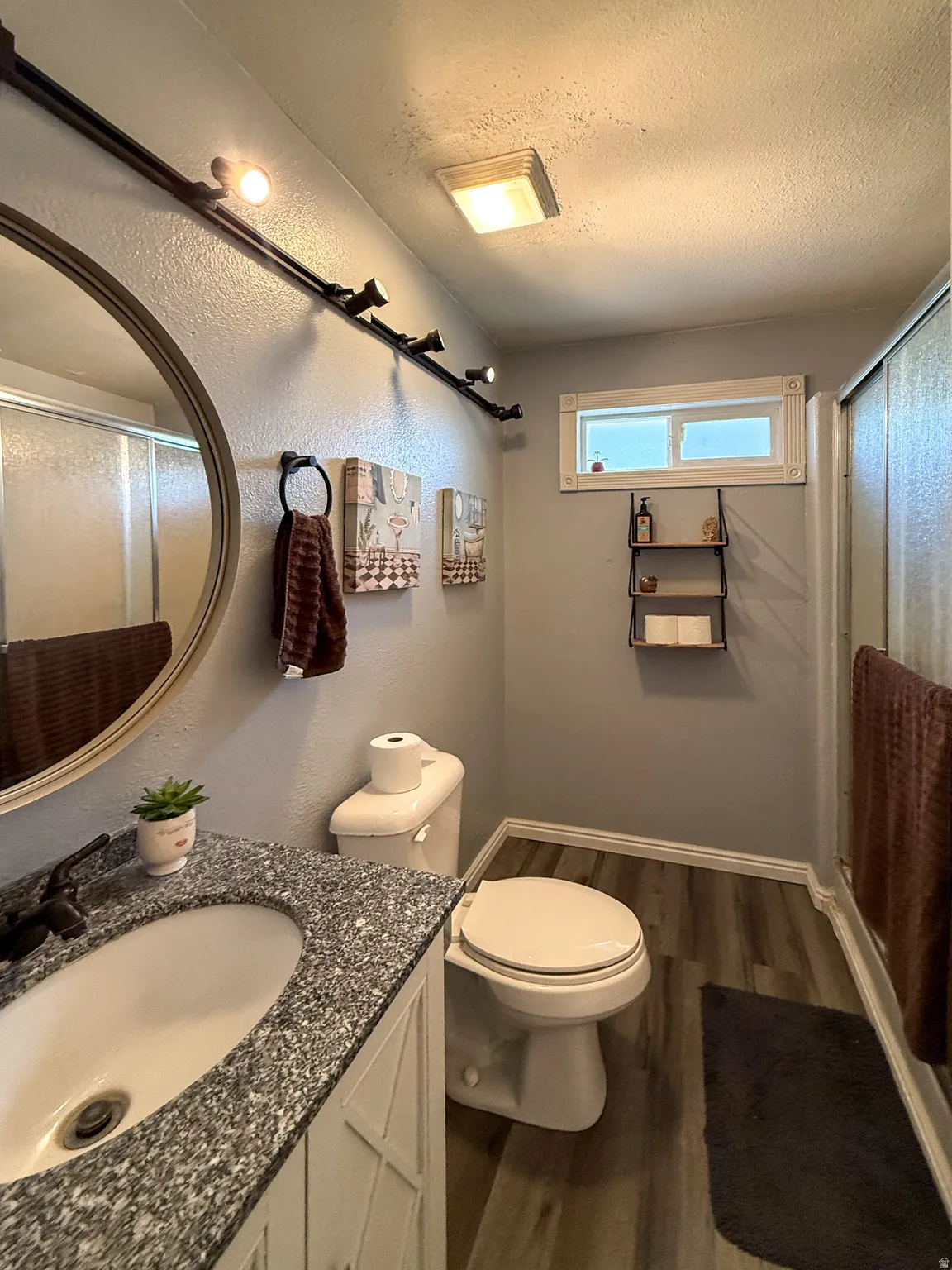 Bathroom featuring a granite-finish countertop, white vanity with decorative paneling, wood-finish flooring, and a white toilet