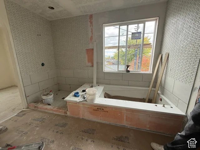 Drop-in bathtub featuring a tiled deck, horizontal ceramic wall tile, mosaic tile accents, and a large window
