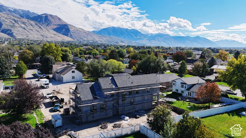 Aerial perspective of a multi-story property under construction featuring a dark shingle roof and a prominent mountain range backdrop