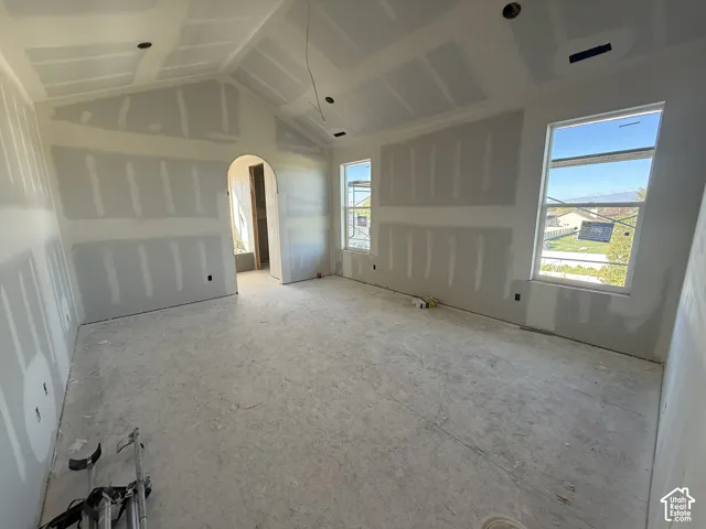 Vaulted ceiling, arched doorway, two windows with white frames, drywall walls, concrete subfloor